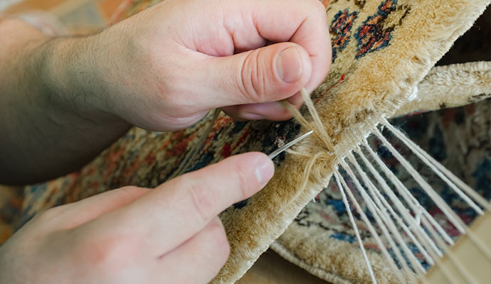 A technician is stitching a binding on an oriental rug.