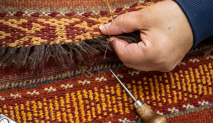 A technician is sewing damaged fringe on an oriental rug.