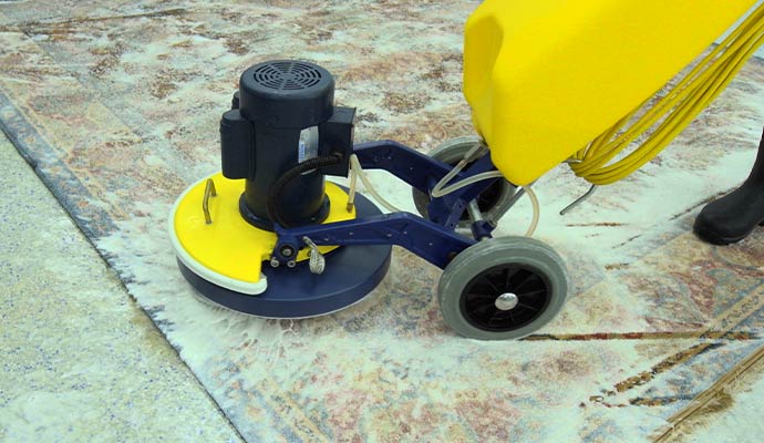 A professional rotary floor machine being used to shampoo and deep clean a large patterned area rug
