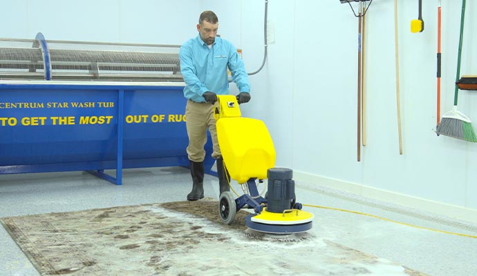 Rug cleaner operating a yellow machine on a dirty rug in a cleaning facility