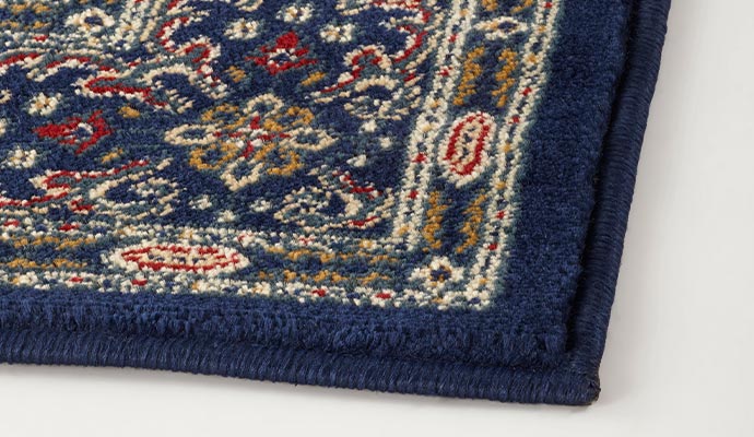 Close-up of a blue patterned rug corner with stitched binding