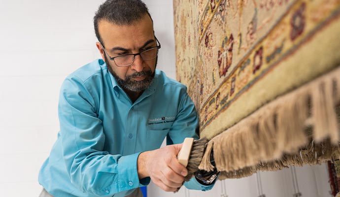 An expert cleaning beige patterned rug using a brush