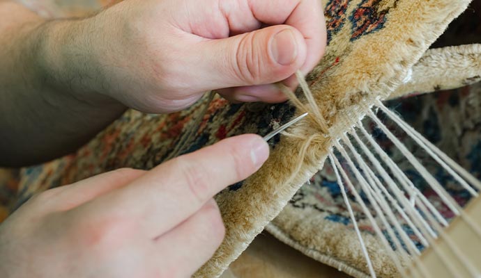 An expert repairing a rug using needle and thread