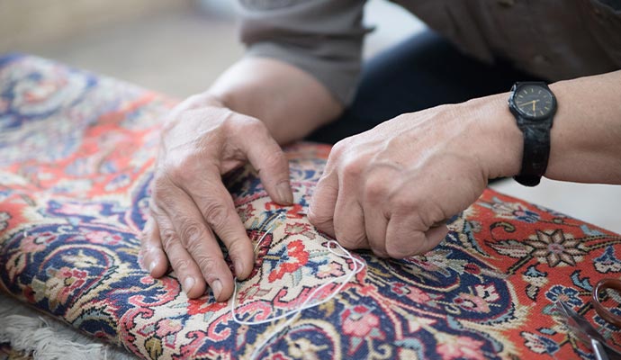 An expert repairing a rug using needle and thread