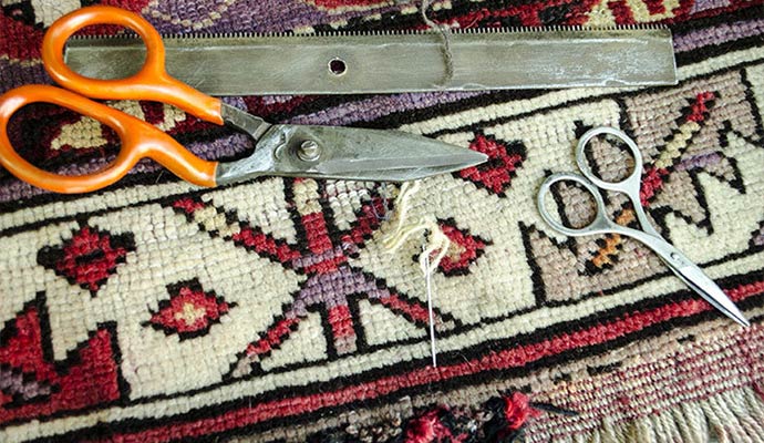 A collection of specialized rug repair tools including heavy-duty shears, small scissors, and a needle on a patterned rug