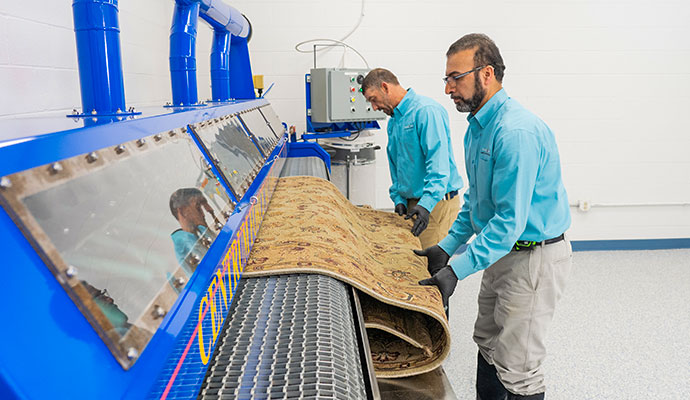 Technician feeding an oriental rug into a specialized cleaning machine