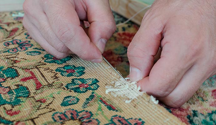 A technician is patching a damaged oriental rug.